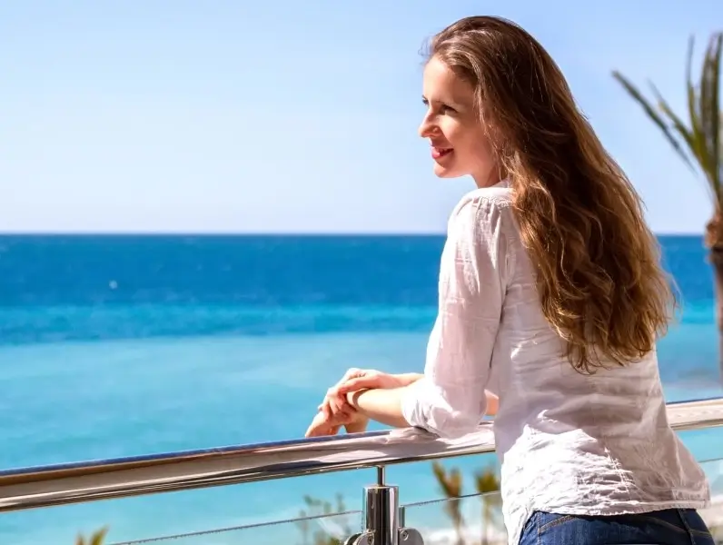 The beautiful girl standing on a balcony of apartments looking at the seaside.